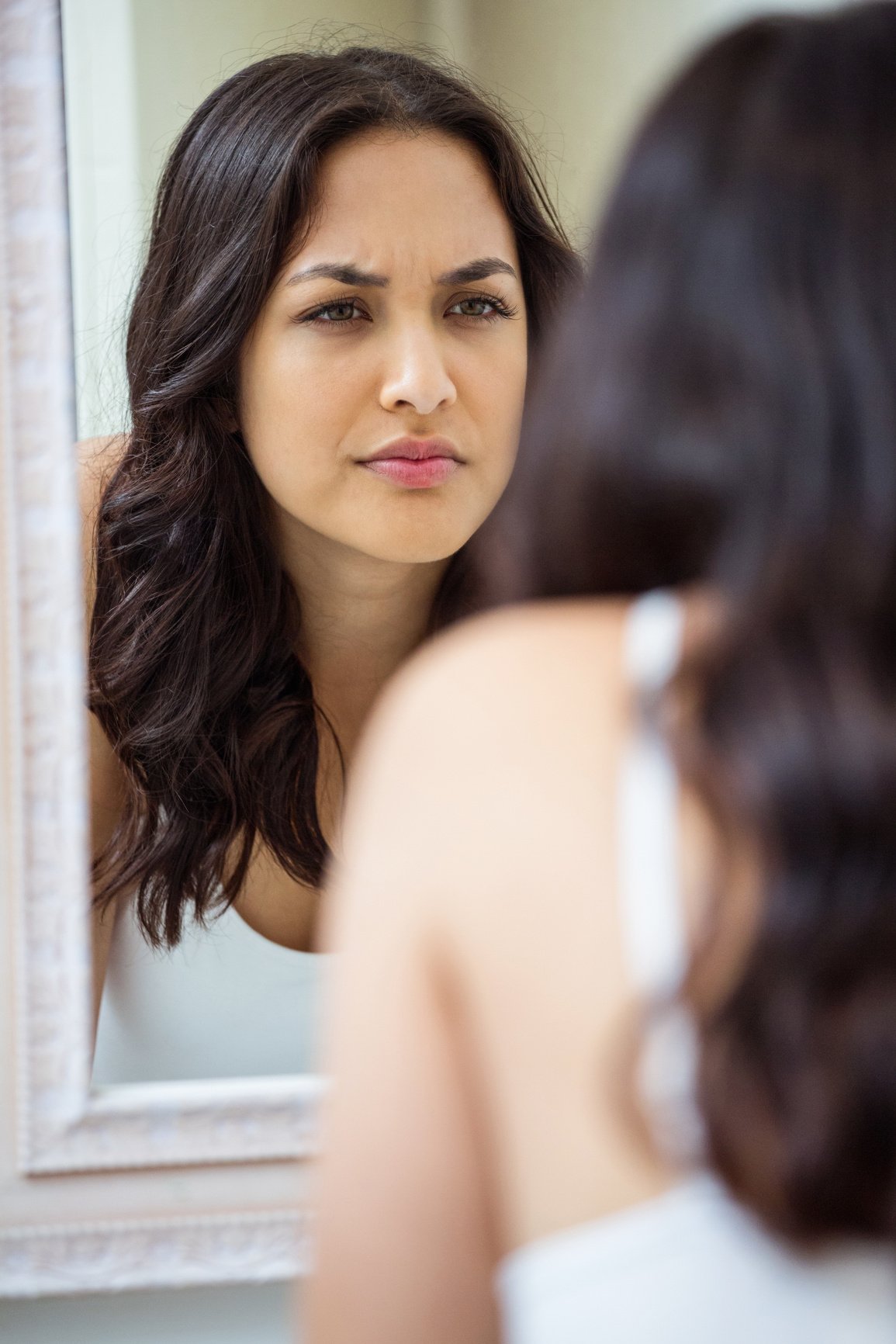 Young woman looking in mirror of bathroom